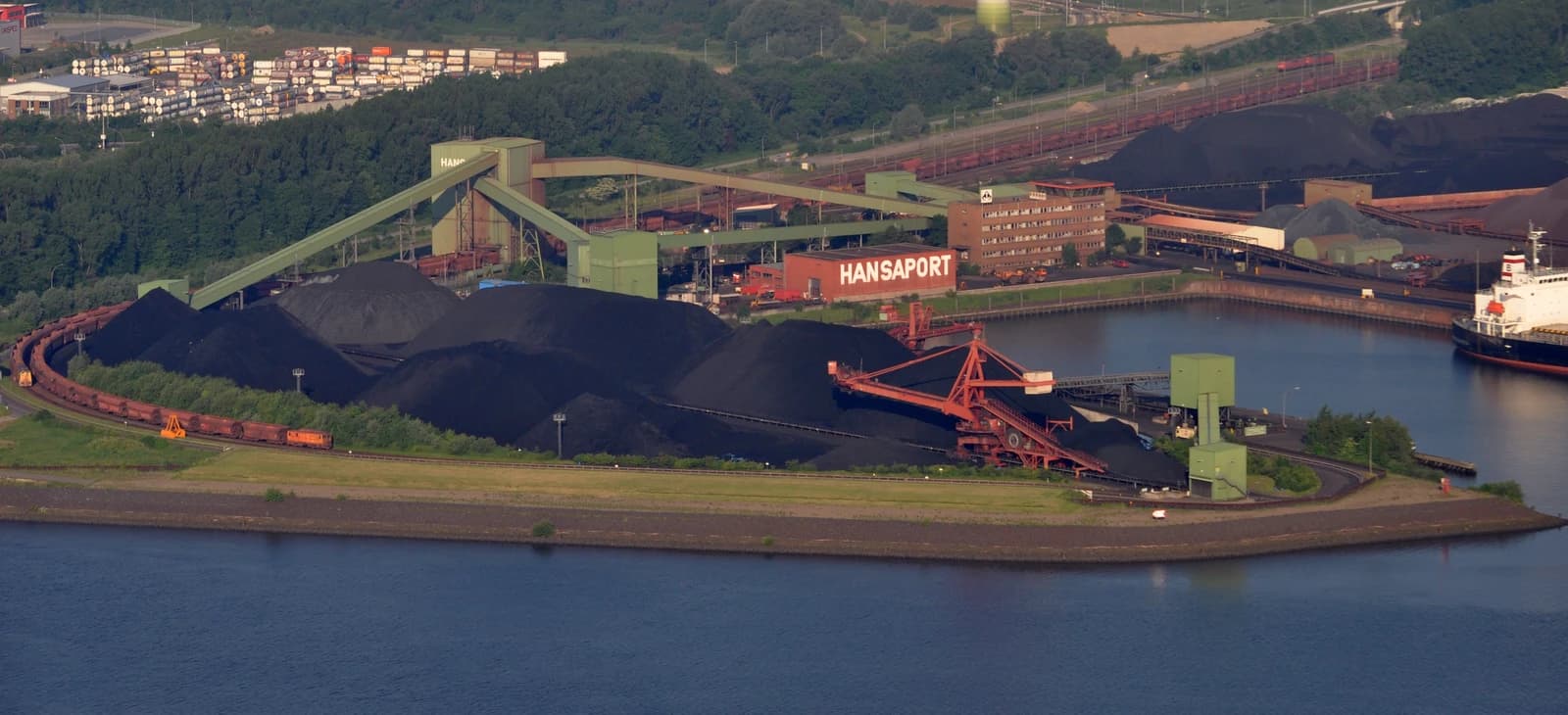Aerial view of Hansaport coal and ore terminal with large coal piles, industrial equipment, and ships.