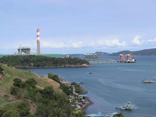 Mariveles Coal-Fired Power Plant with a tall red and white smokestack by a bay.