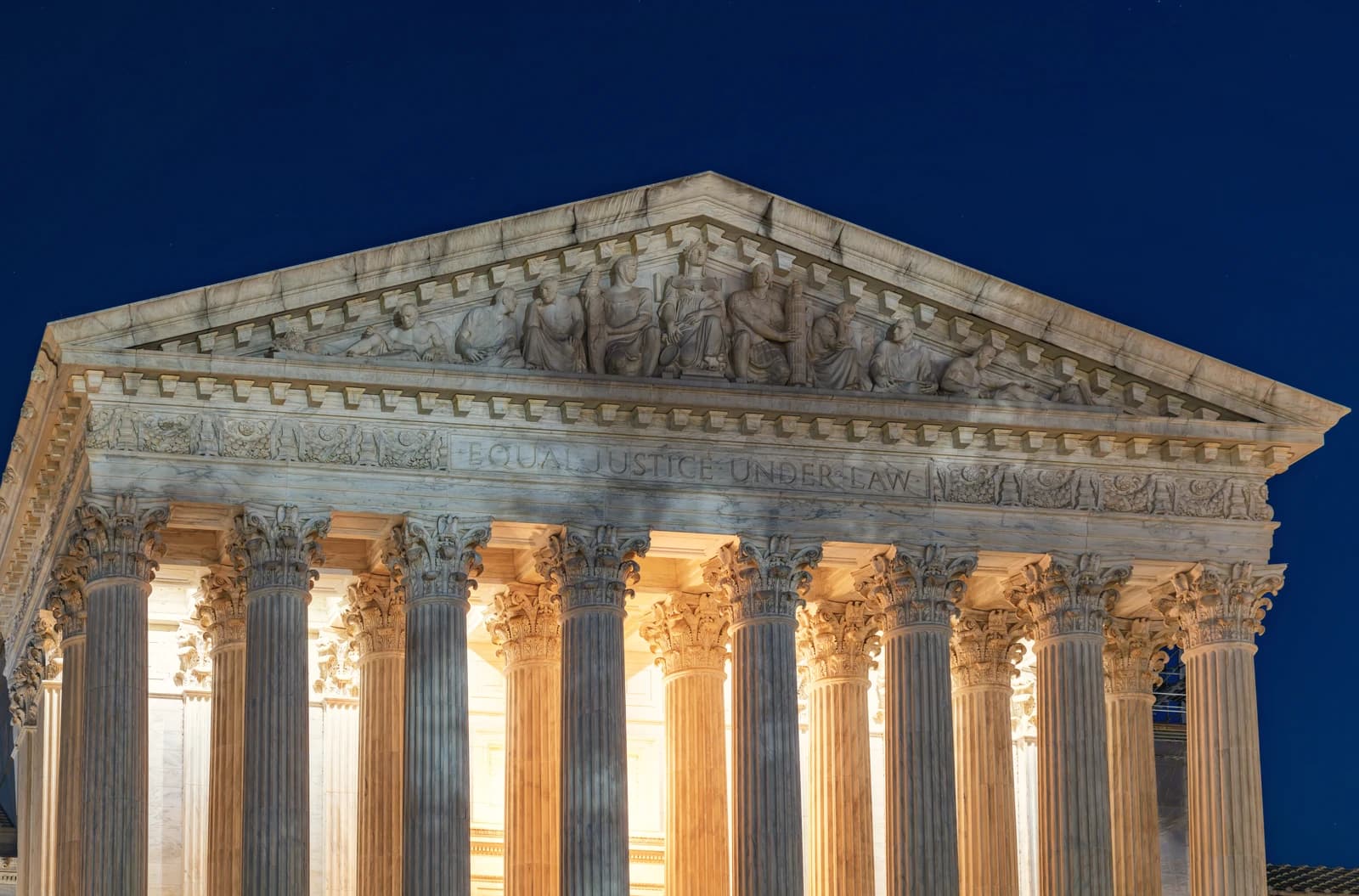 Close-up of the facade of the United States Supreme Court Building at night.