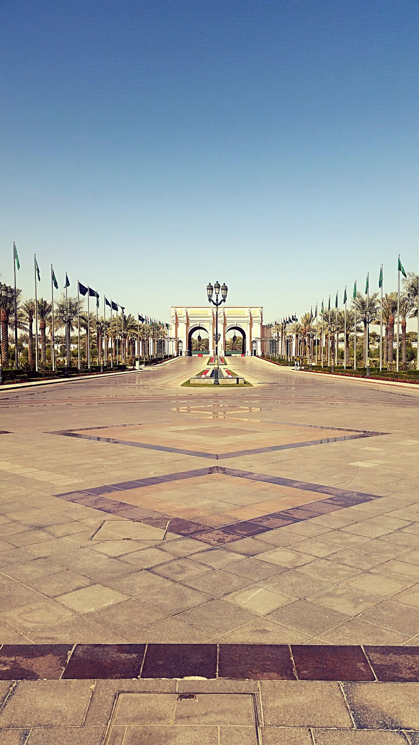 Ritz-Carlton hotel driveway in Riyadh with archway, palm trees, and flags.