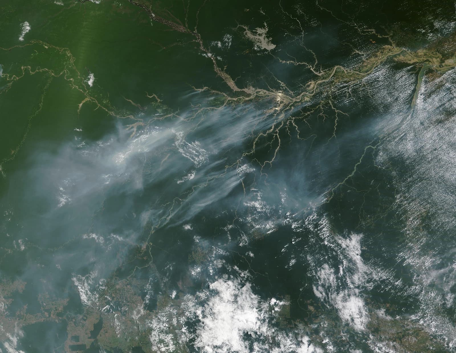 Satellite image showing extensive smoke plumes spreading across a green landscape.