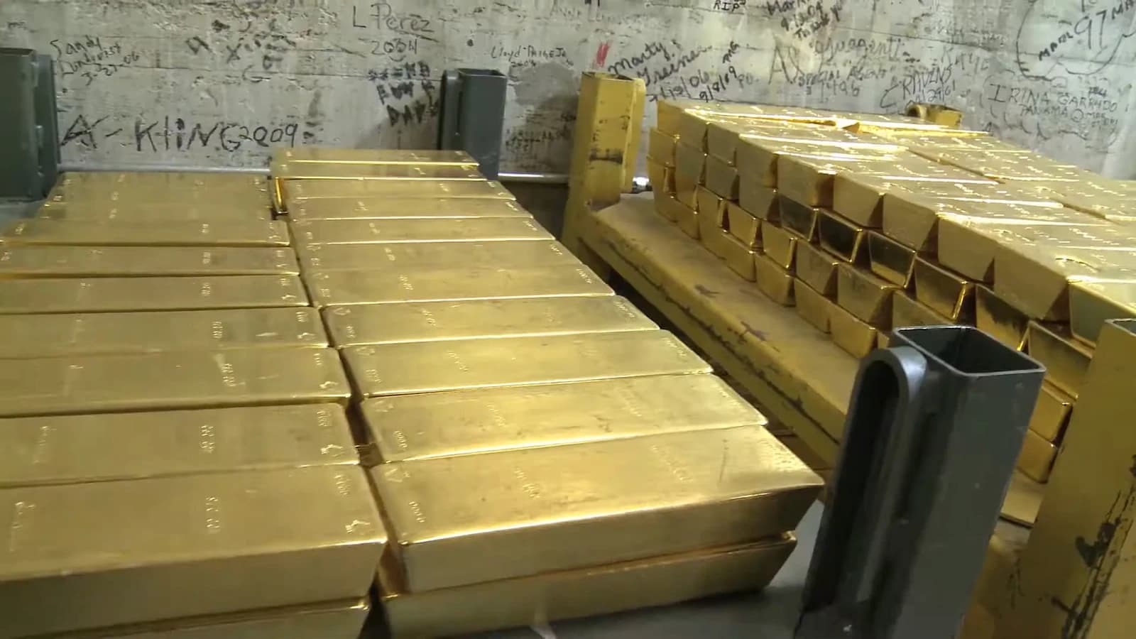 Stacks of gold bars on pallets inside a vault.