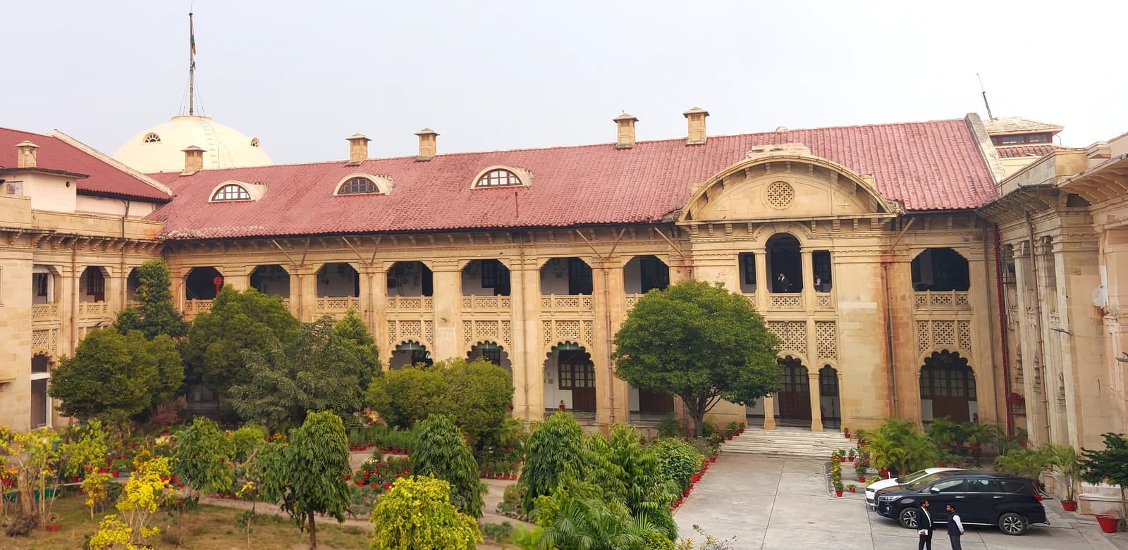 Exterior of Allahabad High Court building with courtyard garden and cars.