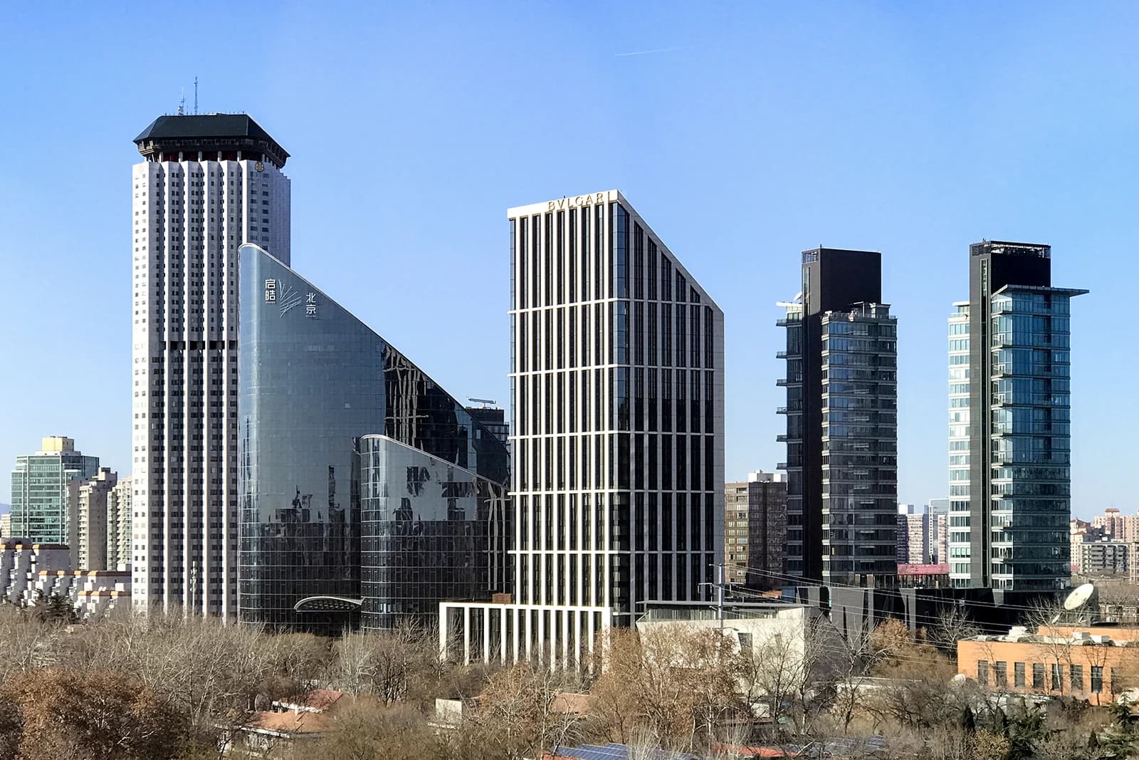 Several modern skyscrapers, including the Bulgari Hotel, stand tall against a clear blue sky in Beijing.