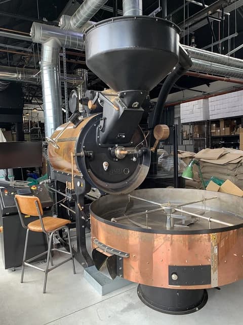 Large industrial coffee roasting machine with copper drum and cooling tray.