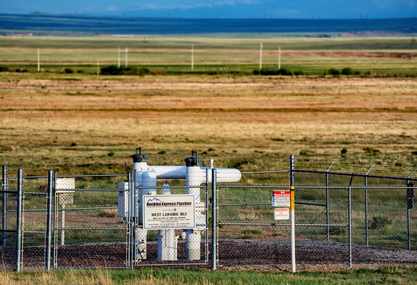 Equipment for the Rockies Express Pipeline visible behind a chain-link fence in a rural landscape.