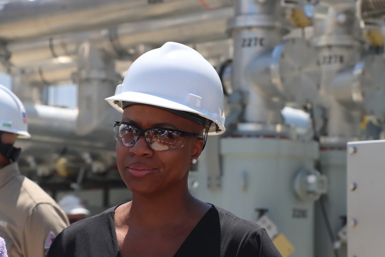 Woman wearing white hard hat and safety glasses looking forward at job site.