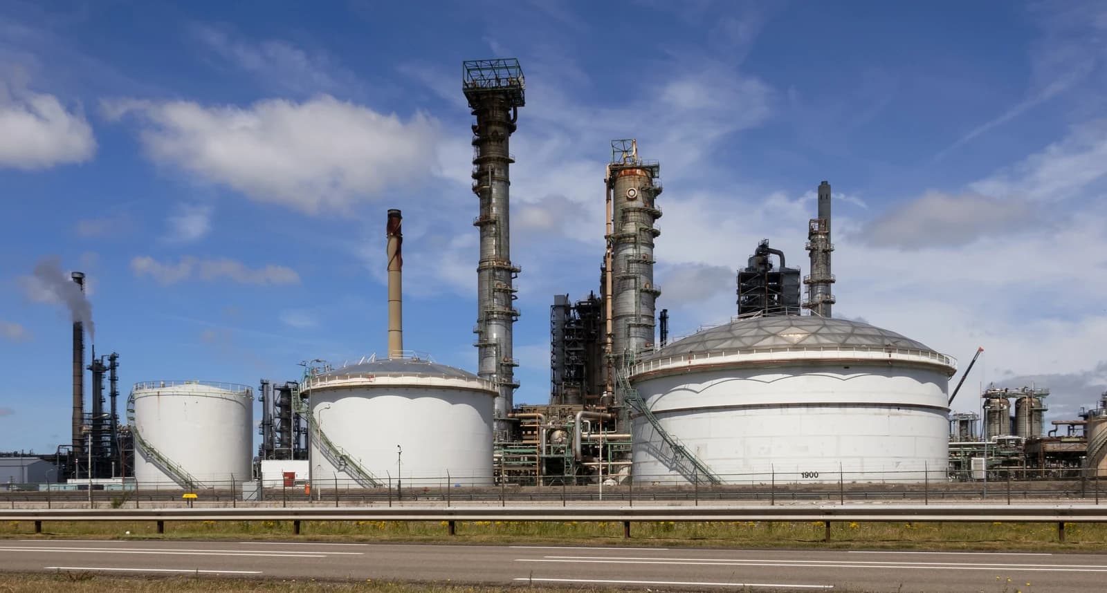 Industrial refinery with large storage tanks and tall processing towers under a blue sky.