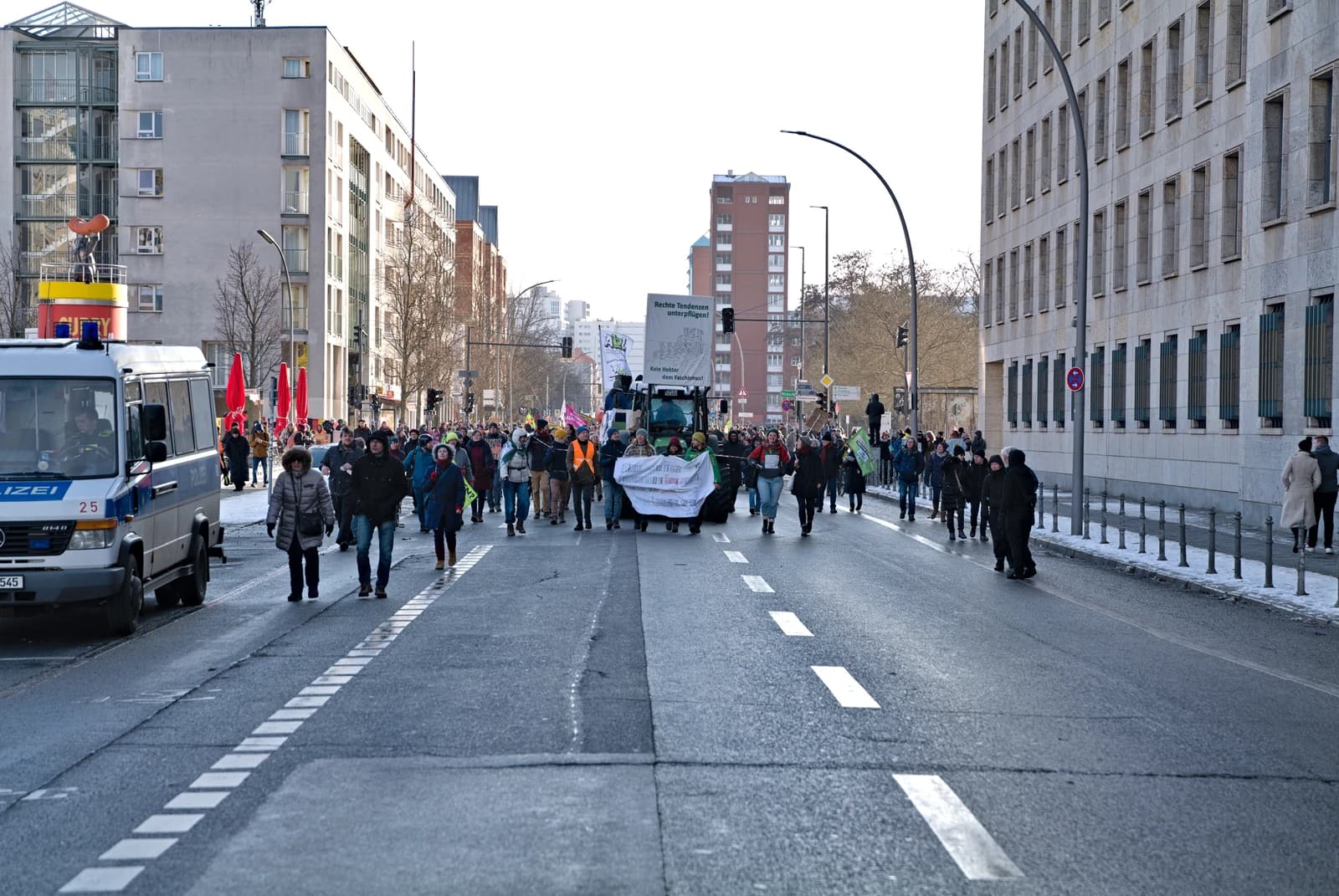 Protesters marching on a city street with a tractor and a police van nearby.