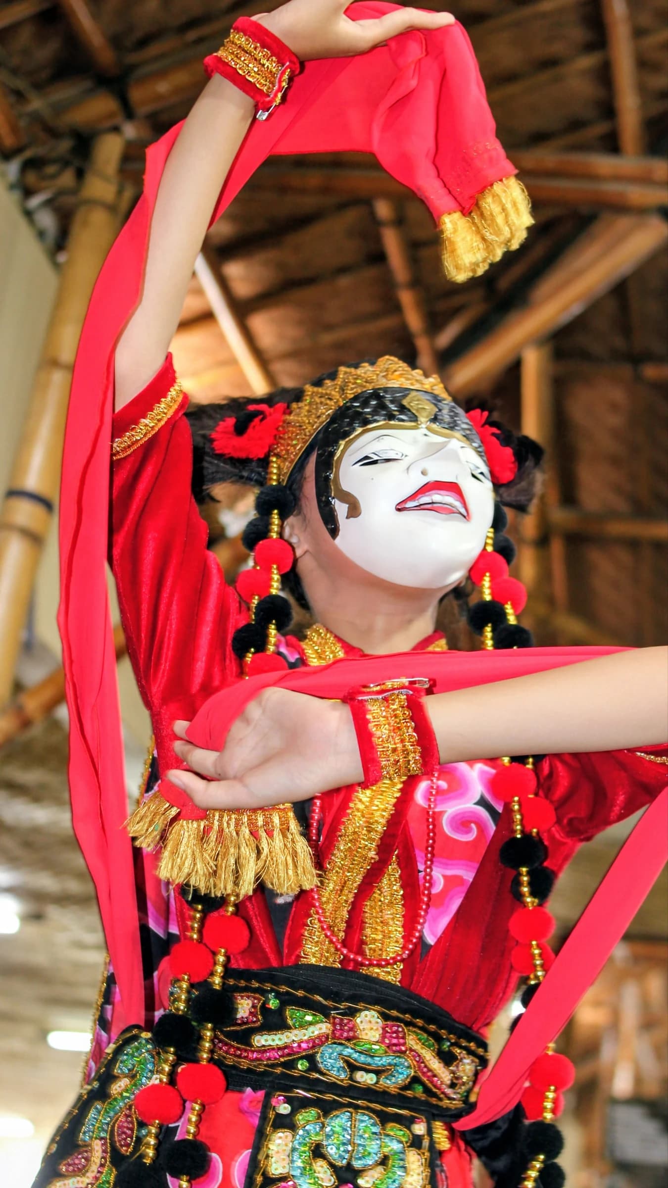 Performer wearing a white mask and red costume with gold accents during an Indonesian dance.