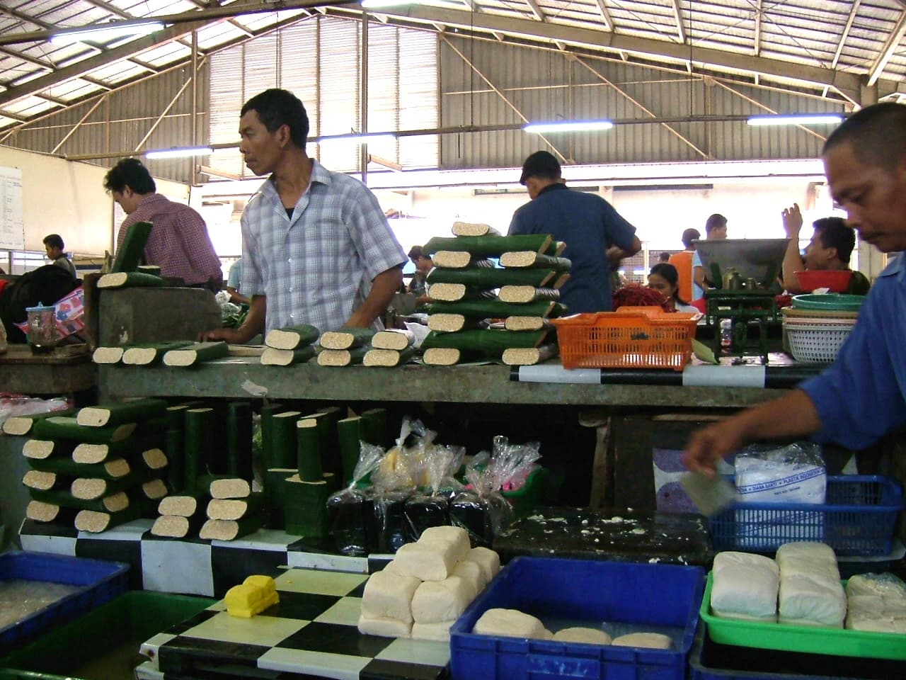 Man in plaid shirt standing behind a market stall selling tempeh and tofu.