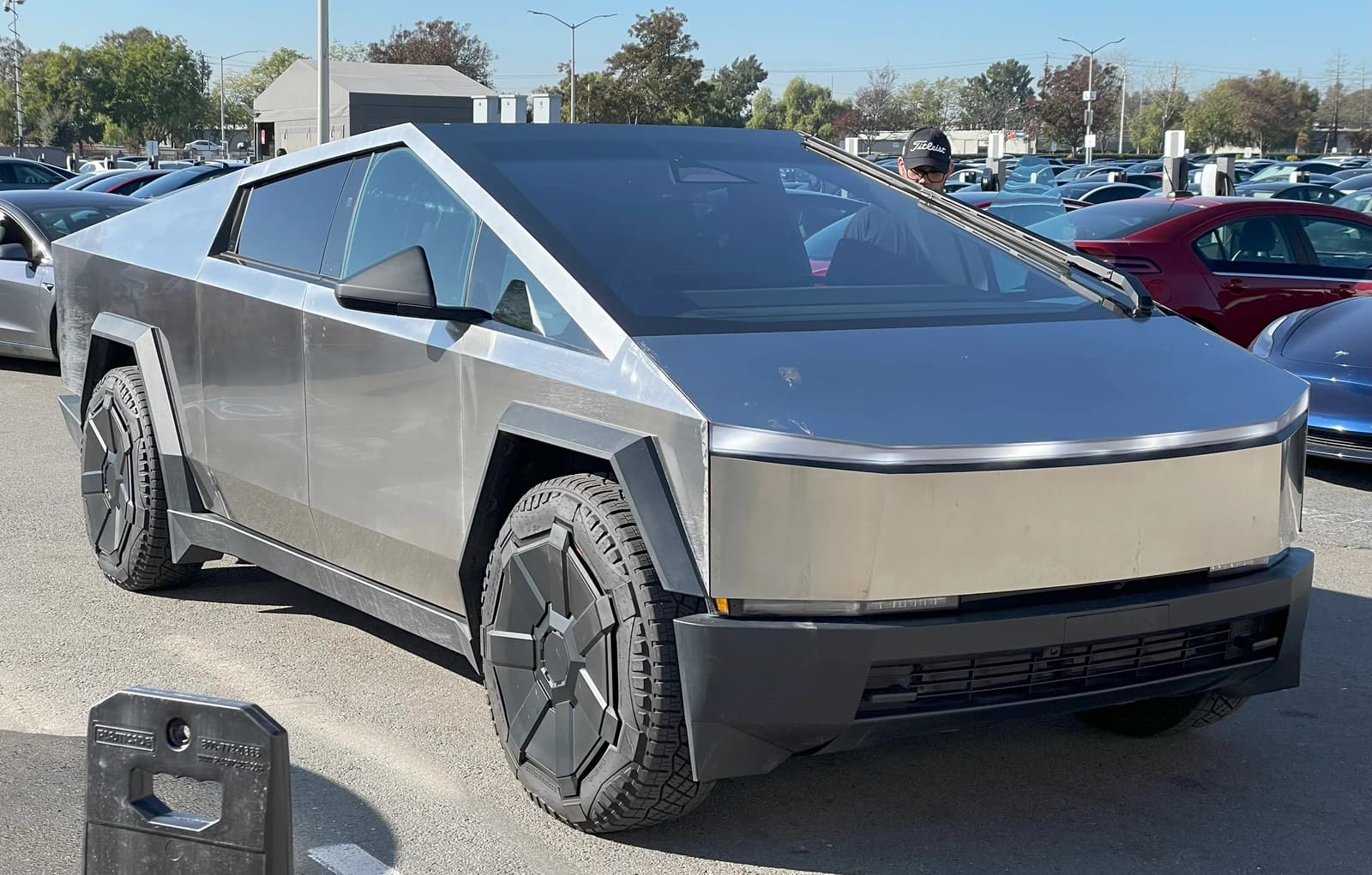 A Tesla Cybertruck parked outdoors in a lot with other vehicles.