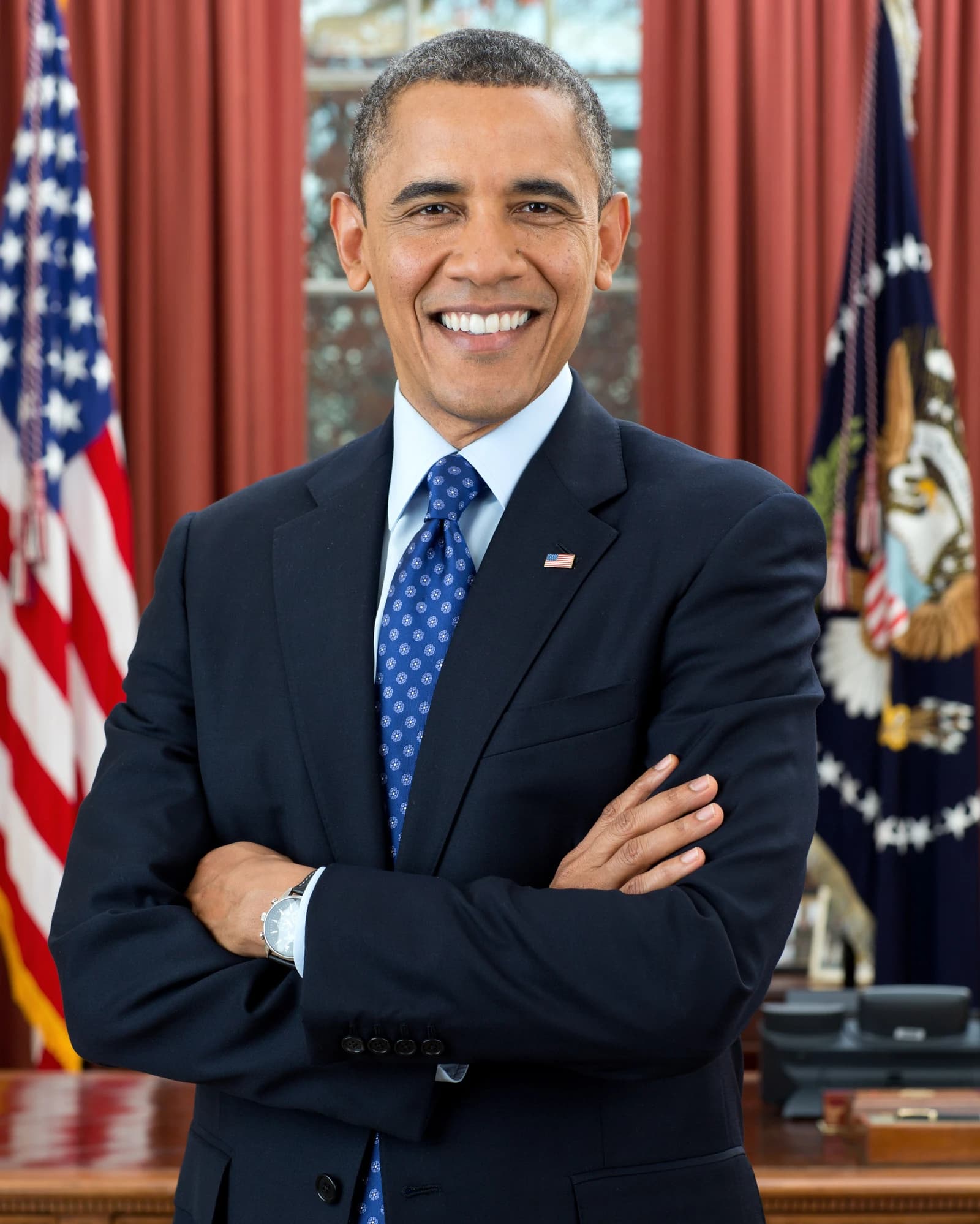 Barack Obama, former President of the United States, smiling with arms crossed.