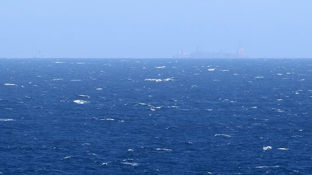 An oil rig seen far off in the distance on a hazy day over the ocean.