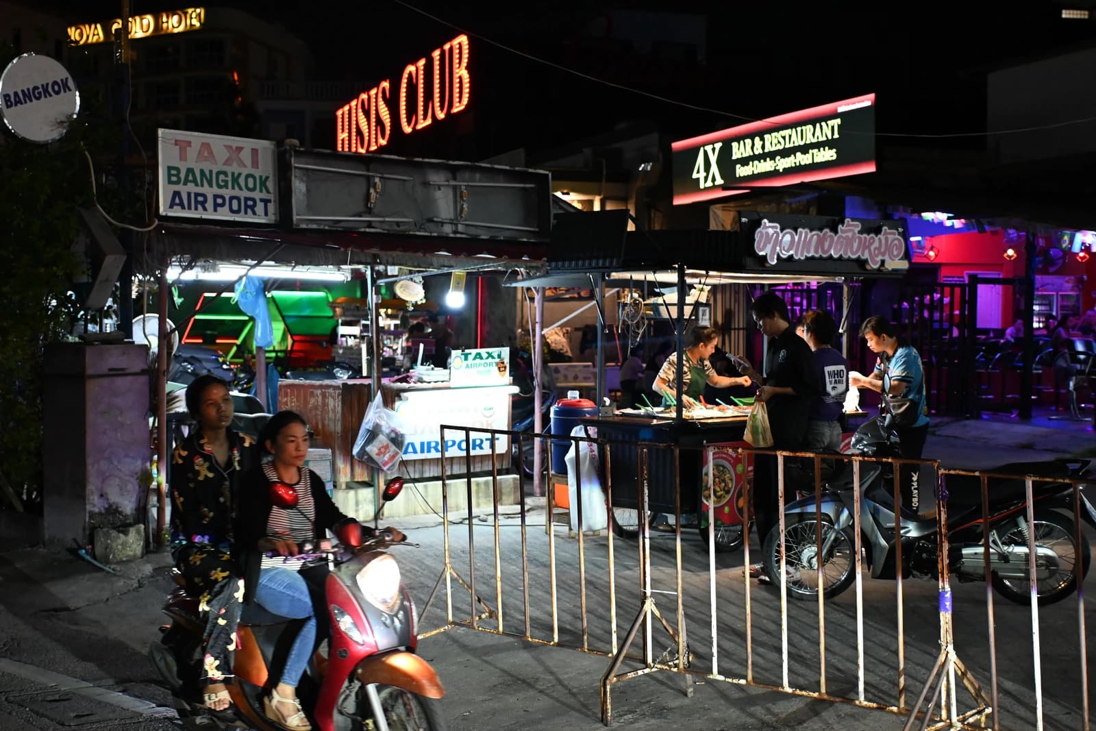 People on motorbikes and others at food stalls on a busy Pattaya street at night.