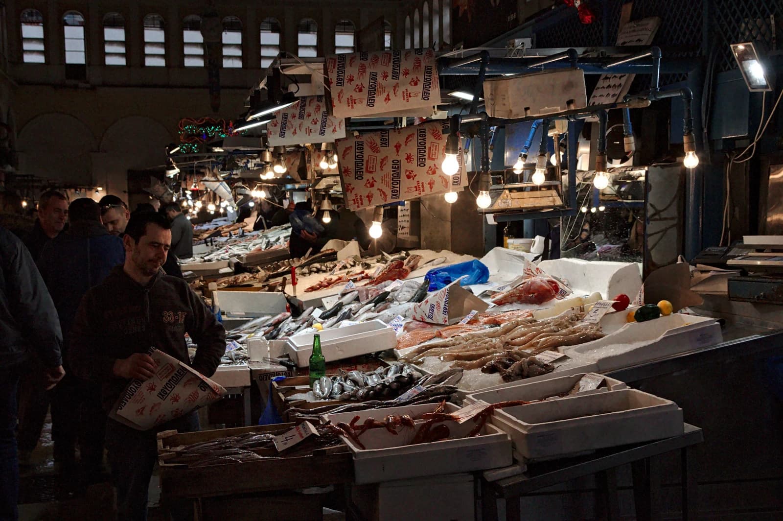 People browse stalls laden with various types of fish and seafood in a market.