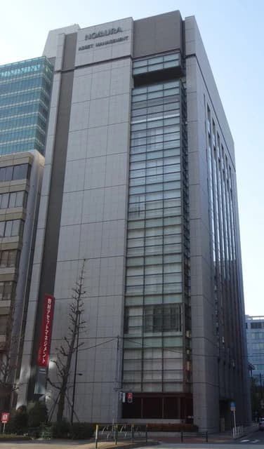 Exterior of the Nomura Asset Management head office building, a tall grey structure.
