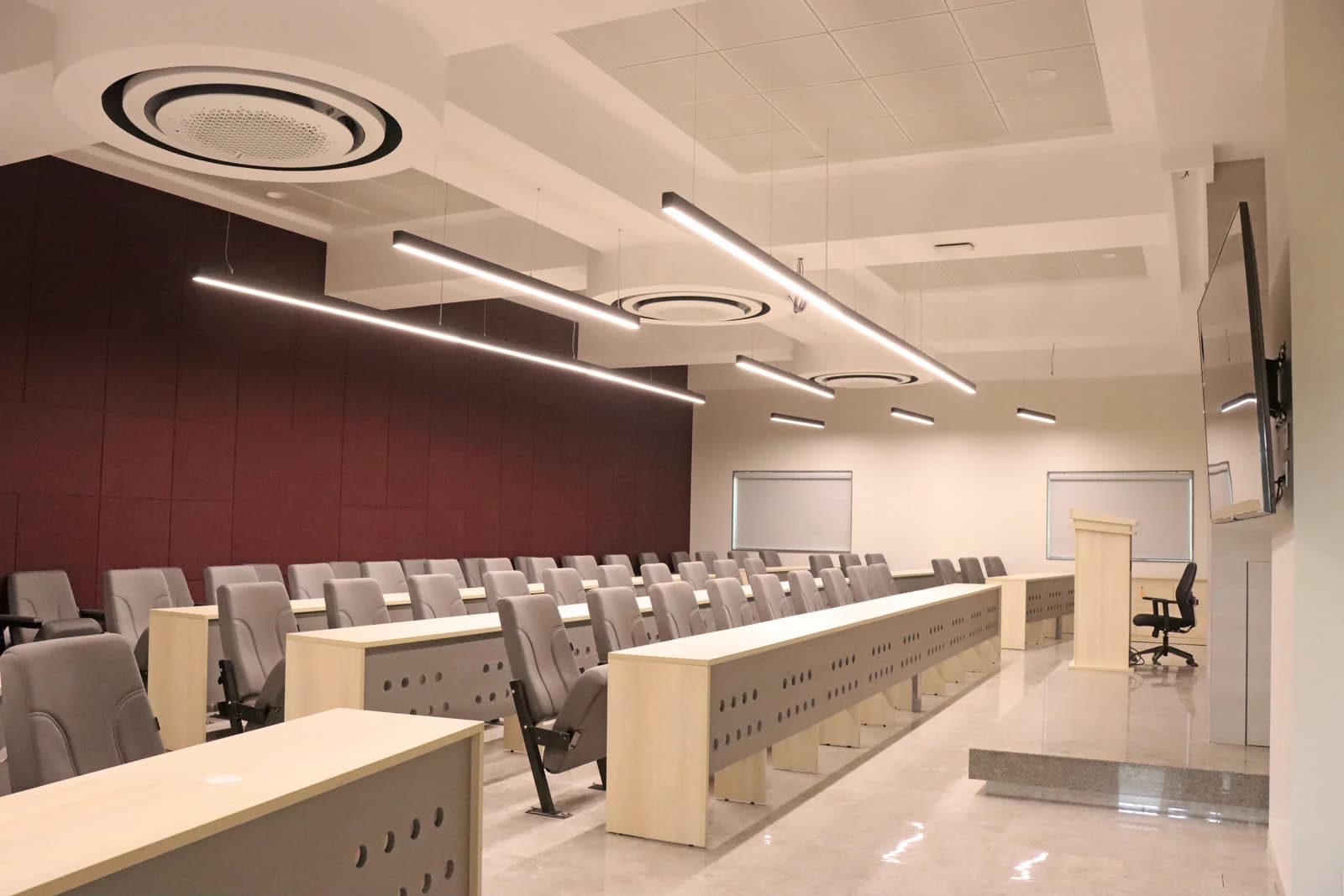 An empty modern classroom with rows of desks, chairs, and a podium at the front.