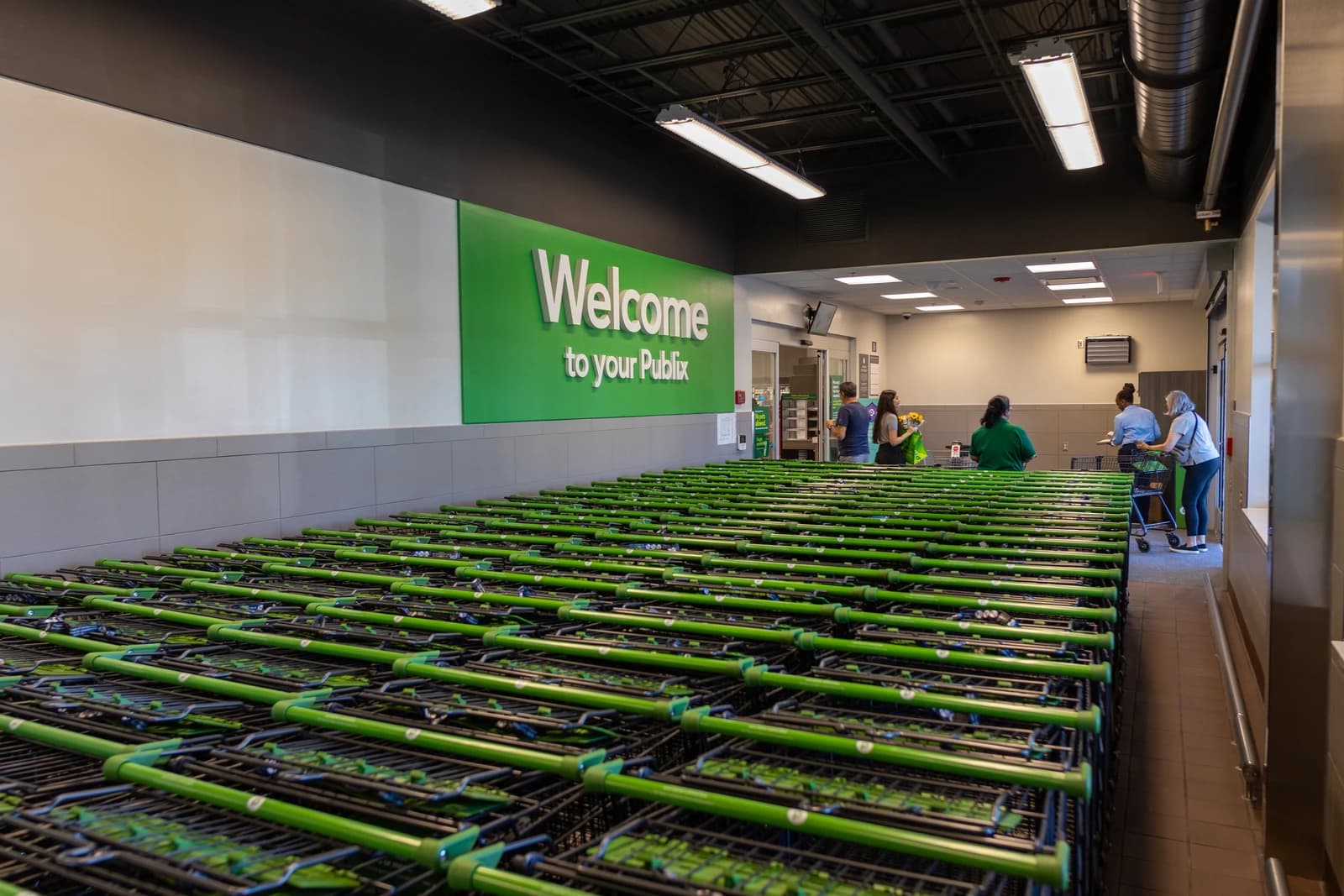 People walking by a large stack of shopping carts inside a Publix grocery store.