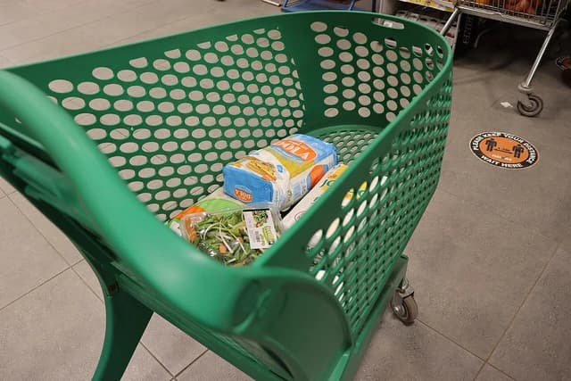 A green plastic shopping cart with a bag of pasta and salad mix inside.