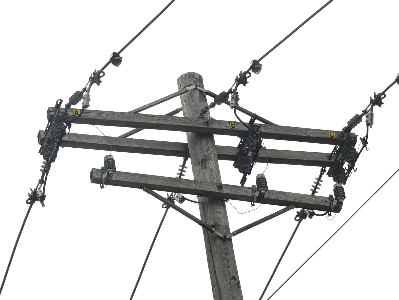 Close-up of utility pole with power distribution lines and insulators against a white sky.