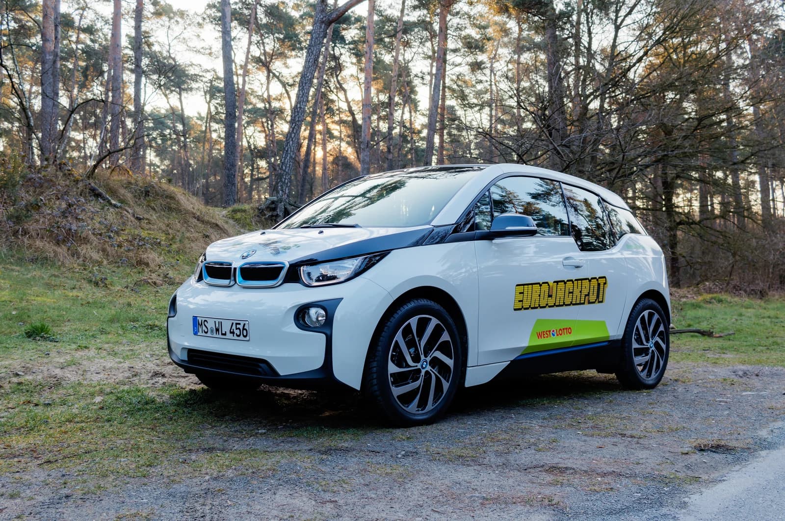A white BMW i3 electric car parked on a dirt road in a wooded area.