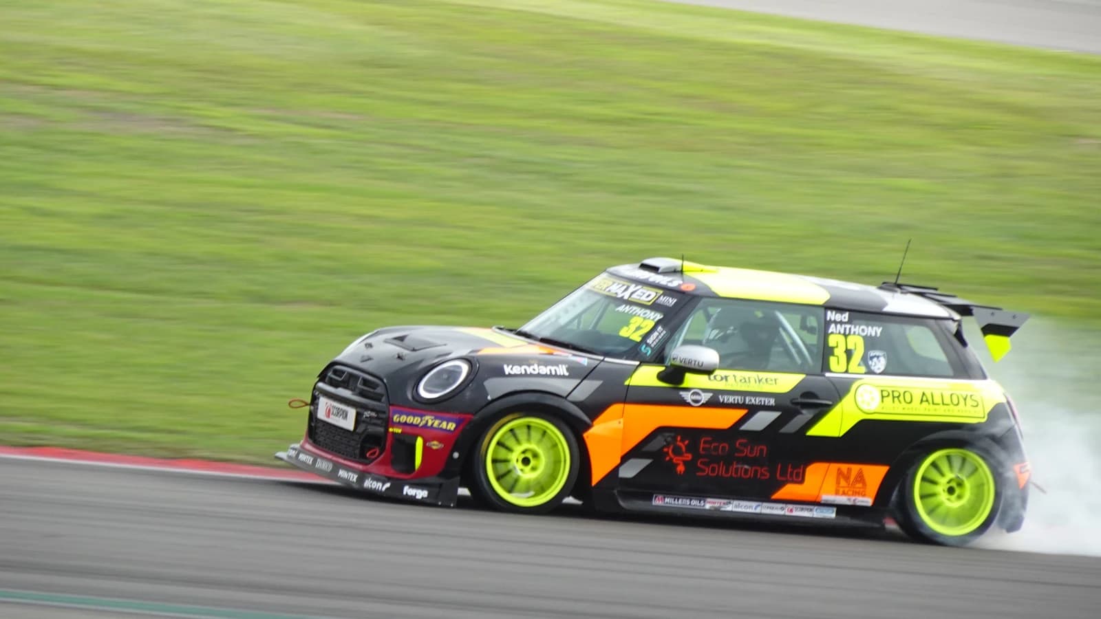 A black and yellow MINI racing car with the number 32 drifting on a racetrack.