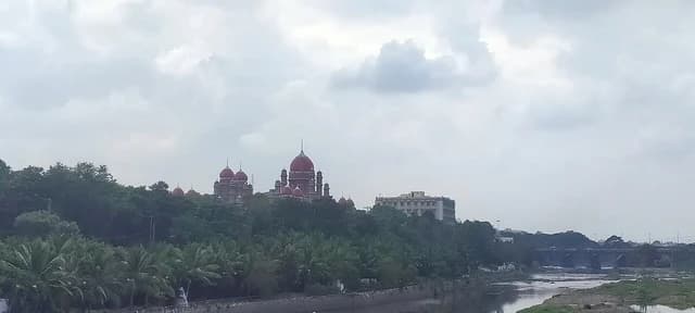 High Court building with red domes, surrounded by trees, overlooking a river.