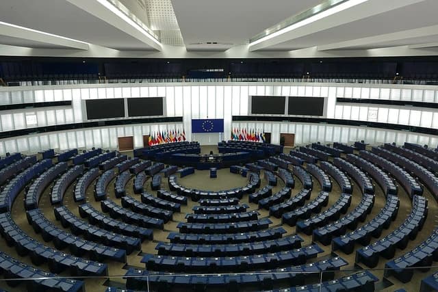 Empty European Parliament hemicycle in Strasbourg with European Union and member state flags.