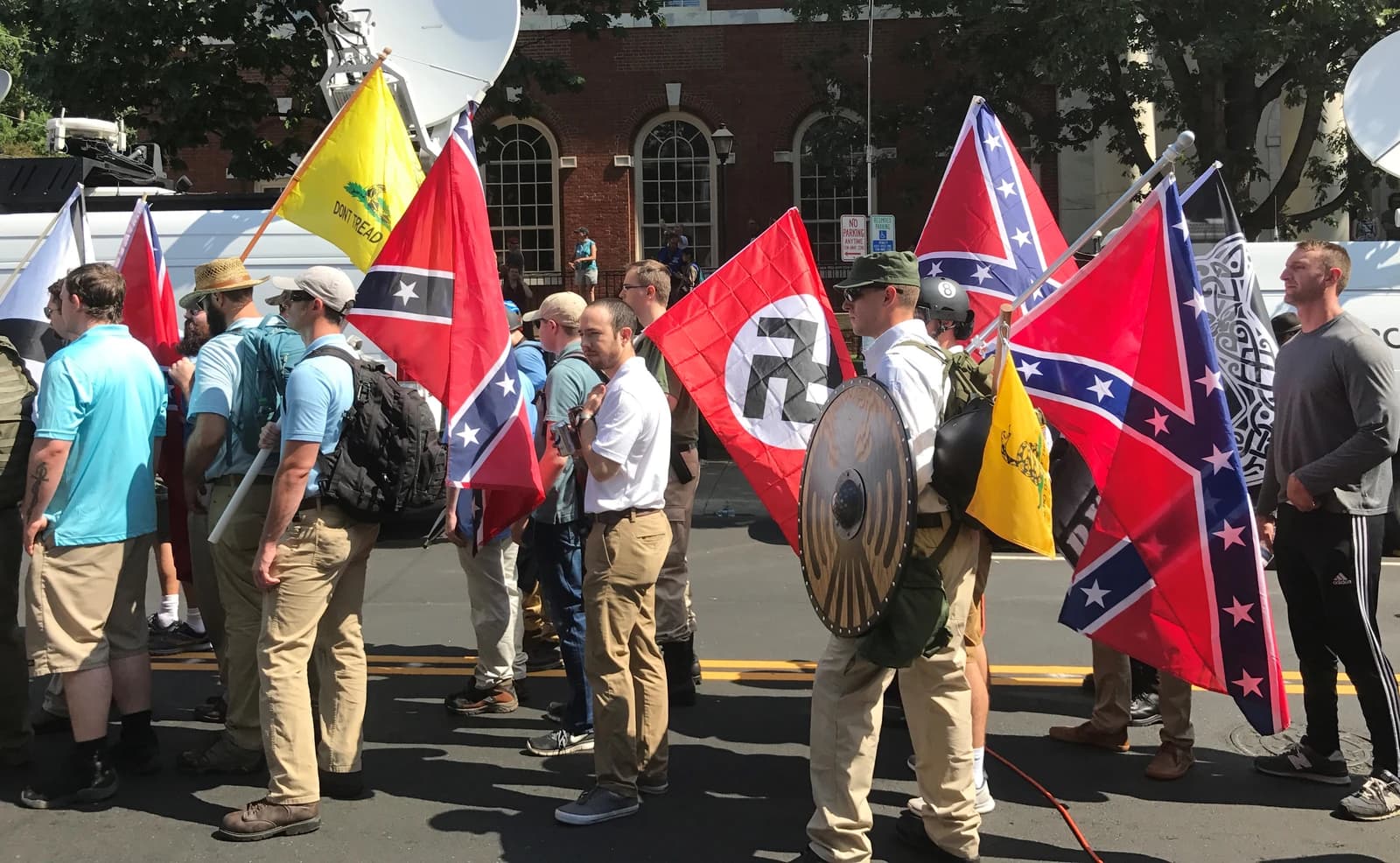 Protestors holding Confederate, Gadsden, and Nazi flags at a rally.