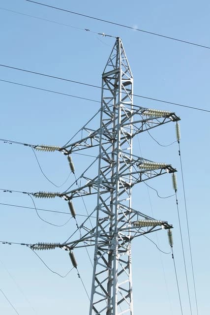 An electric transmission power tower stands against a clear blue sky, illustrating electricity infrastructure.