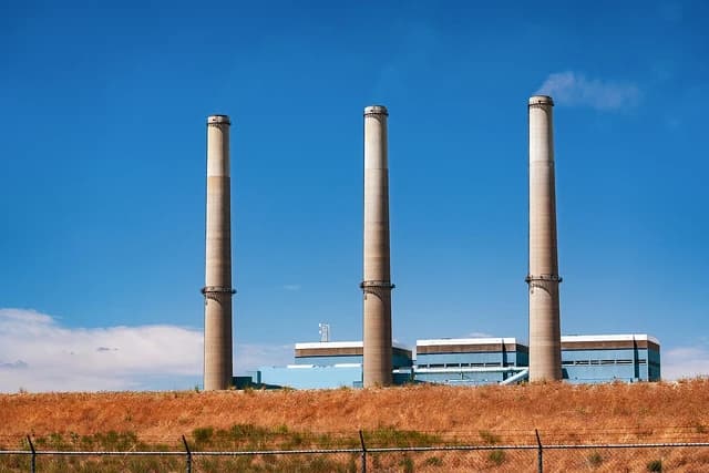 Three tall smokestacks stand over a coal-fired power plant building.