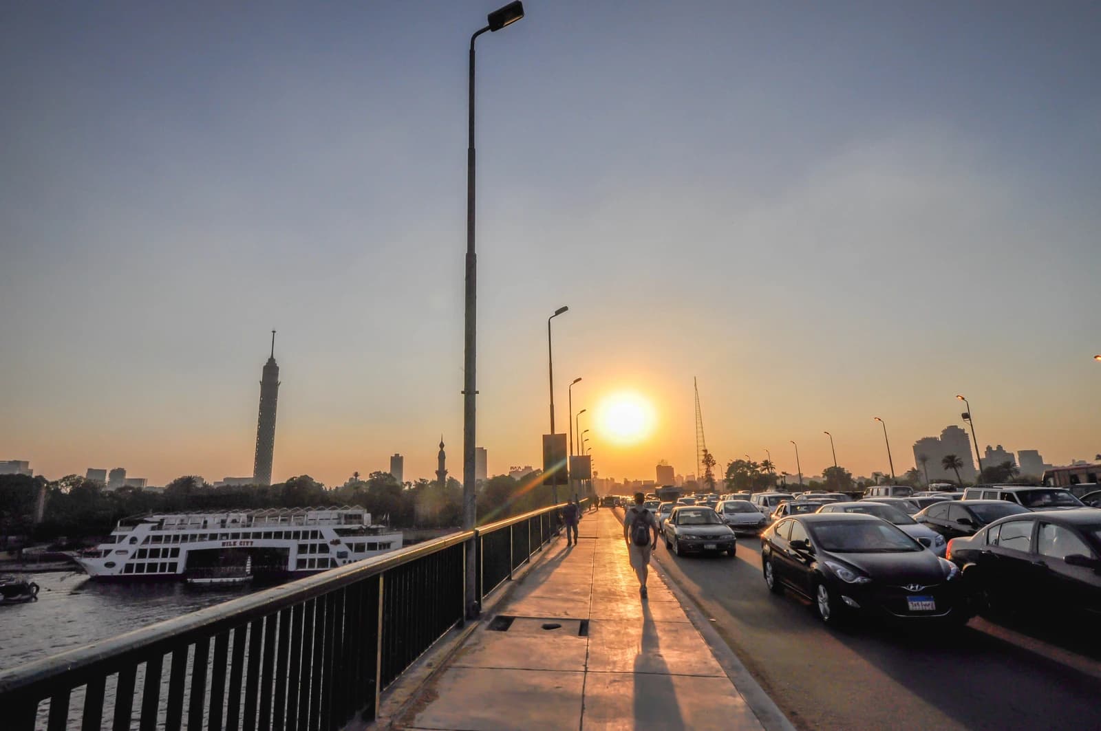 Traffic and pedestrians on 6th of October Bridge with Cairo Tower visible in the distance.