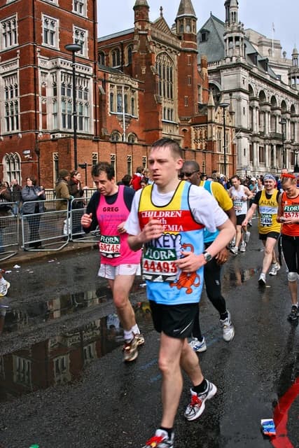 Runners in colorful bibs on a wet road with historic buildings in the background.