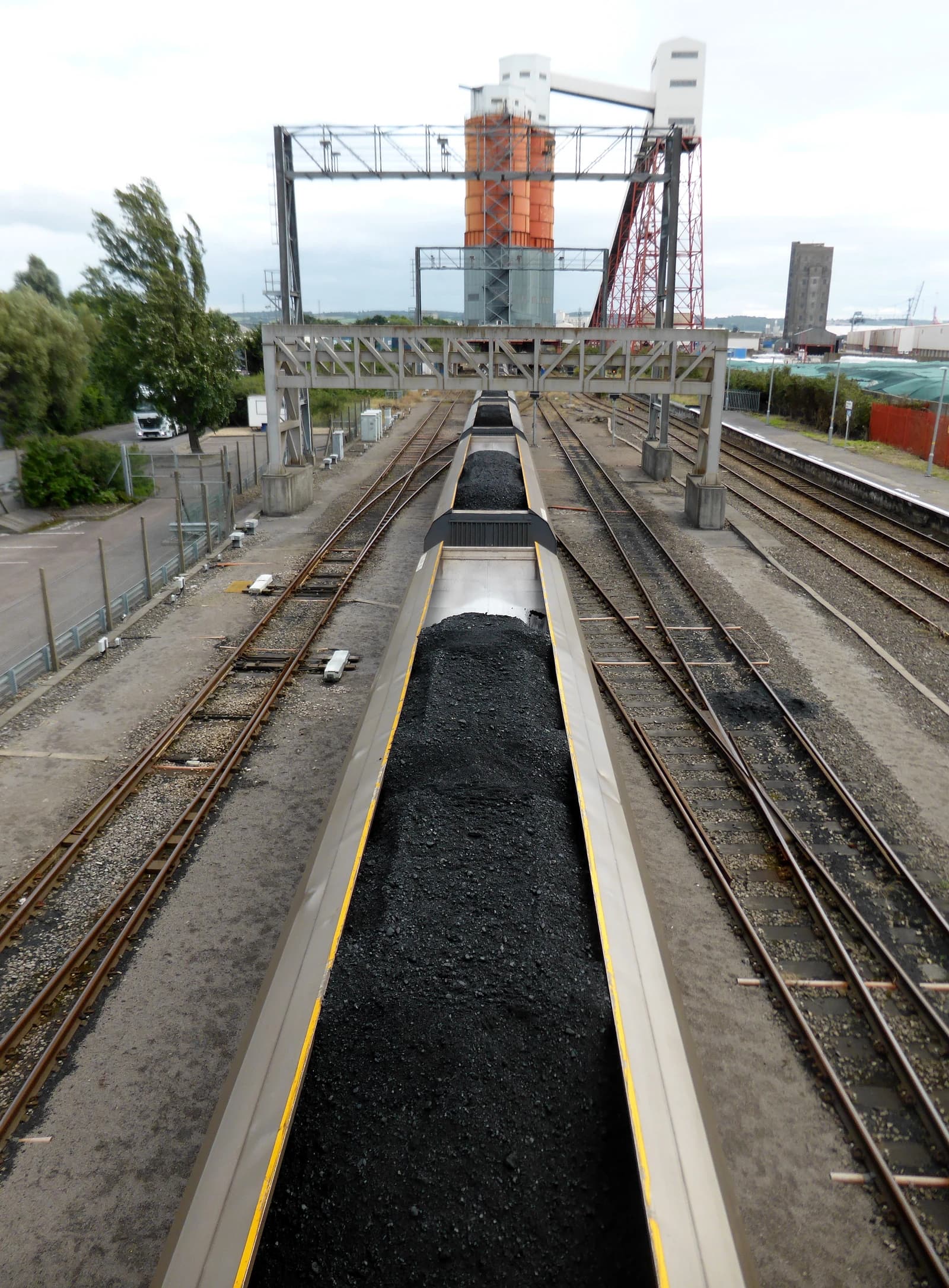 Several railway freight wagons loaded with coal on parallel tracks next to industrial buildings.