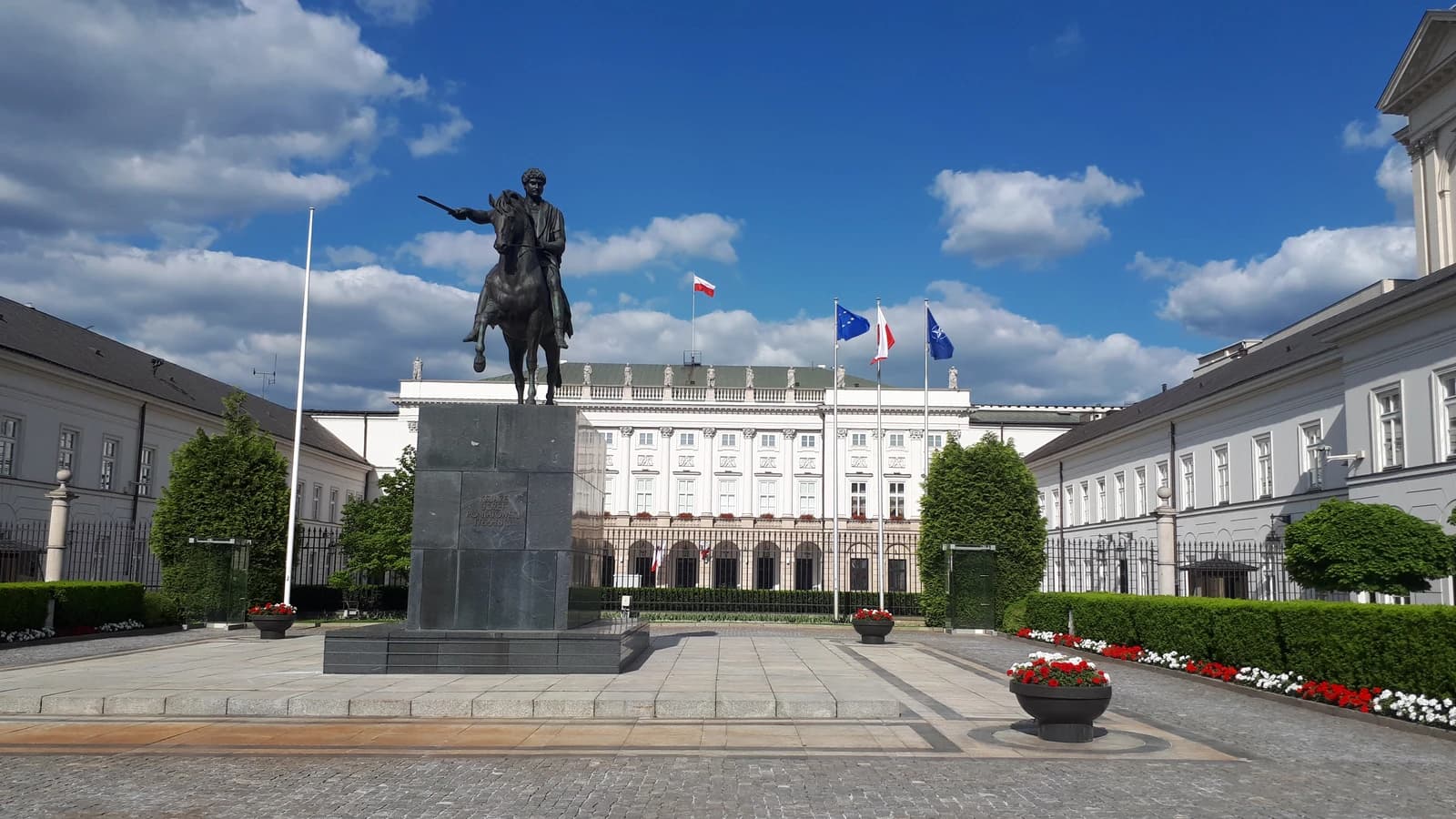 Presidential Palace in Warsaw, Poland, with a statue and flags outside.