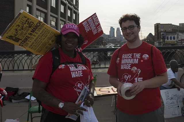 Two individuals, a woman and a man, holding signs at a minimum wage rally.
