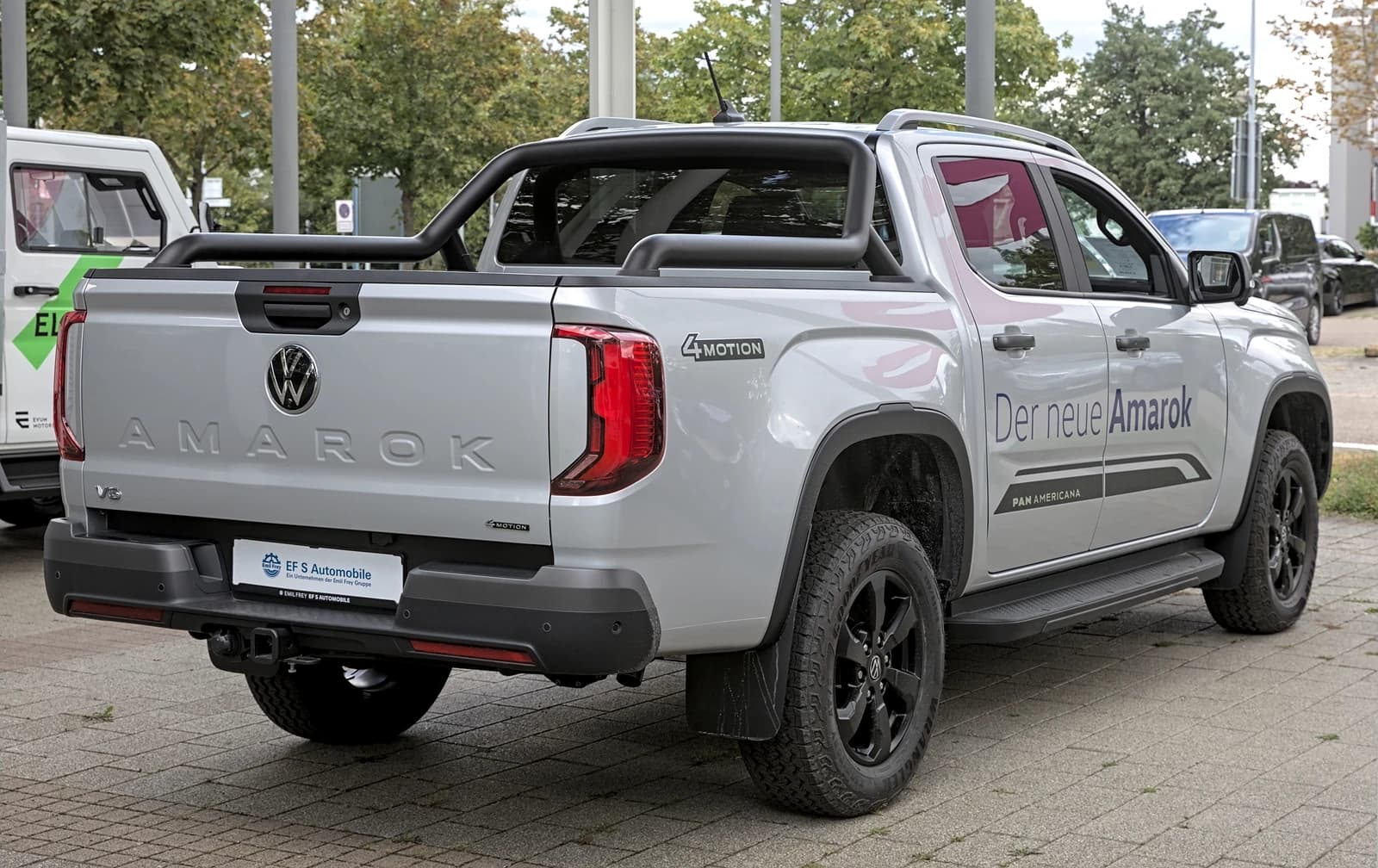 Silver Volkswagen Amarok pickup truck with black wheels and roll bar, parked outdoors.