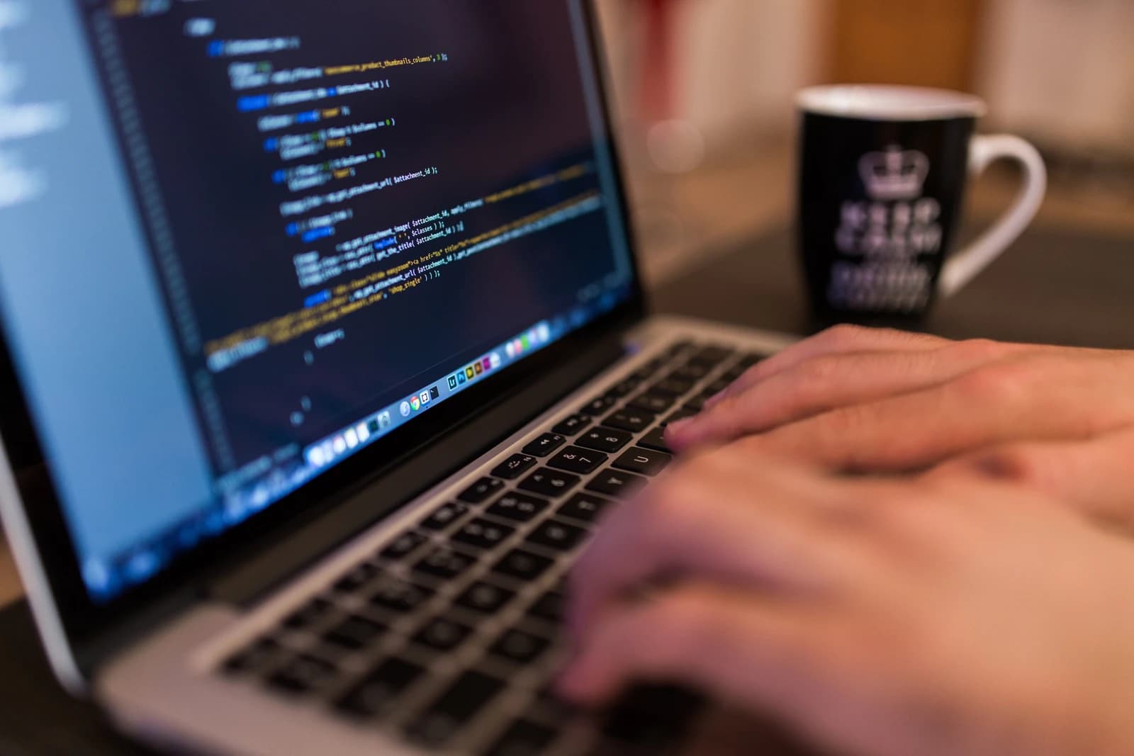Programmer's hands typing on a laptop computer, displaying lines of code on the screen.