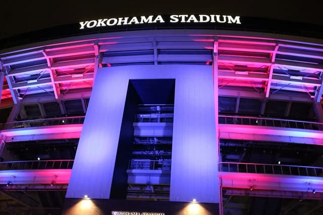 Yokohama Stadium exterior at night, illuminated with pink and blue lights.