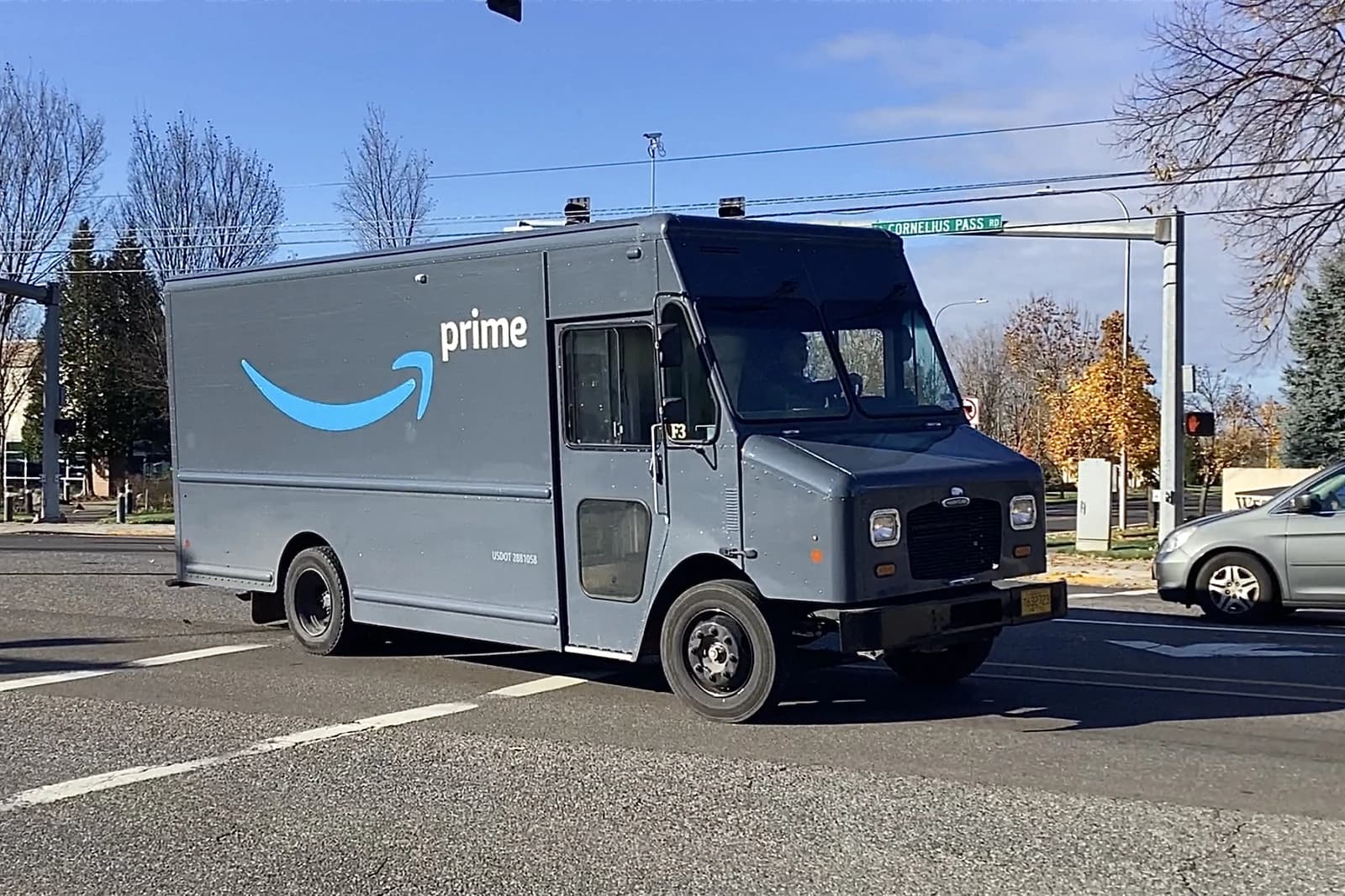 An Amazon Prime delivery truck drives on a paved road during the day.