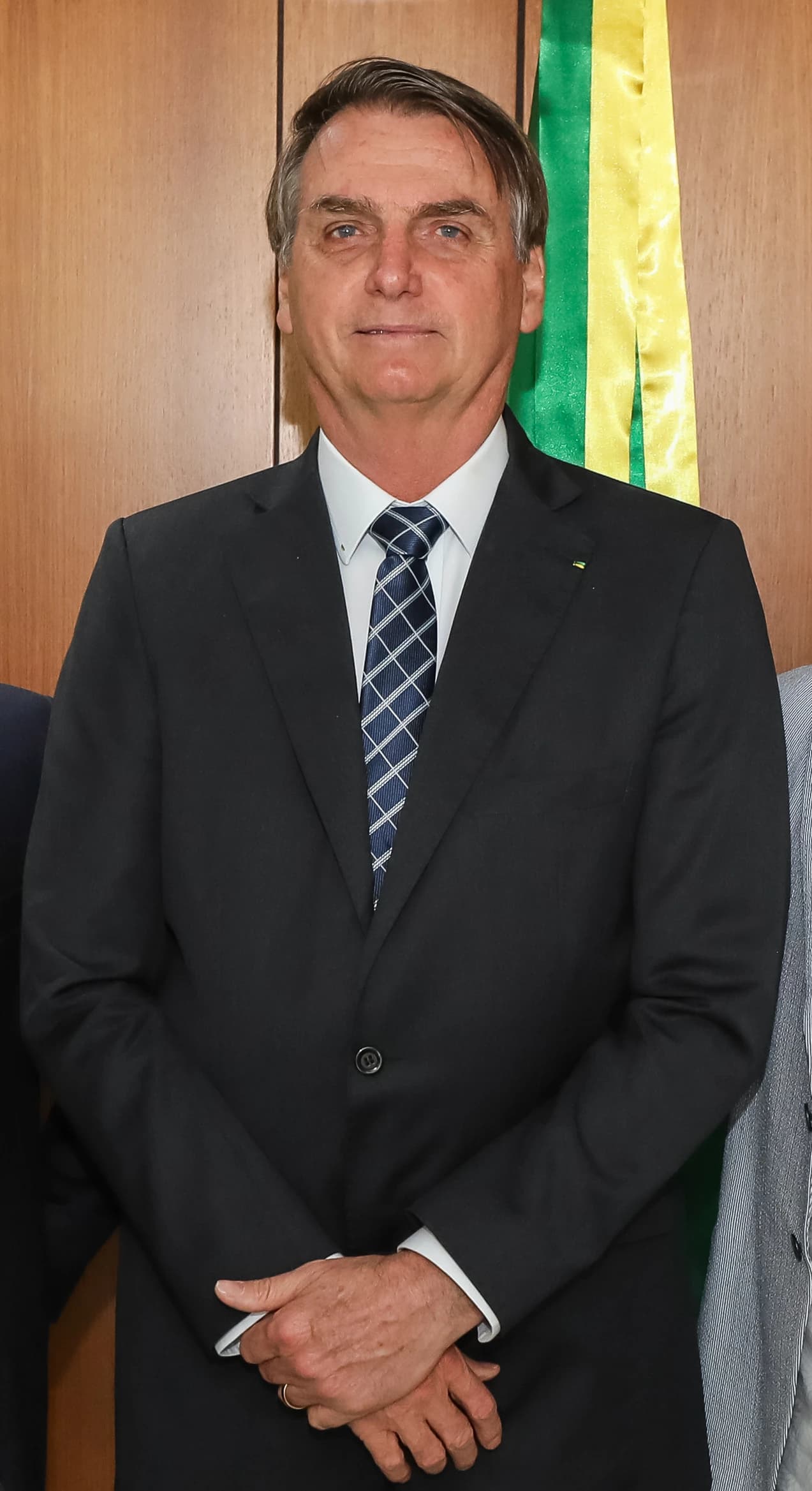 Jair Bolsonaro, former President of Brazil, stands formally in front of a wood wall.