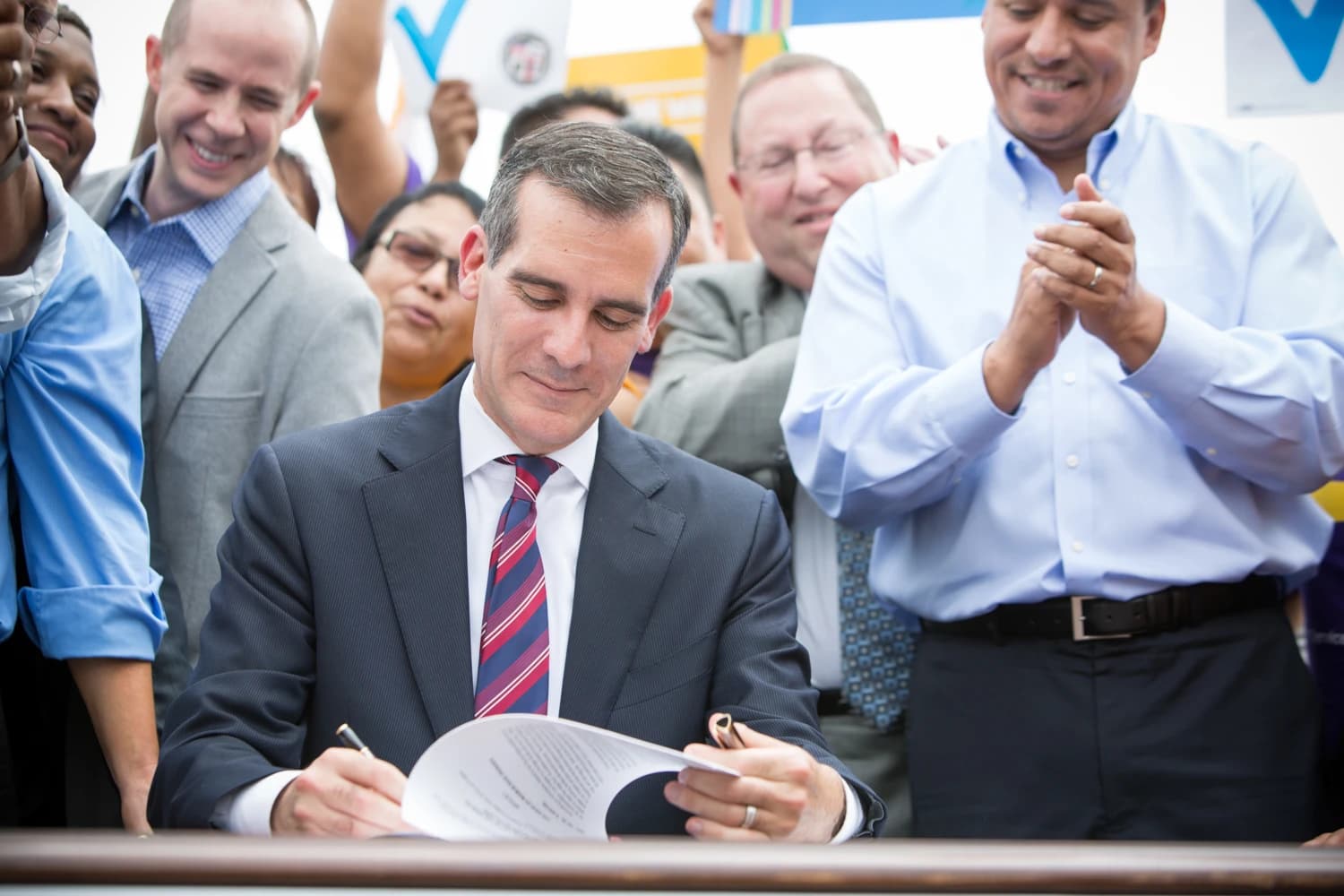 Eric Garcetti, Mayor of Los Angeles, signing a document at a podium.