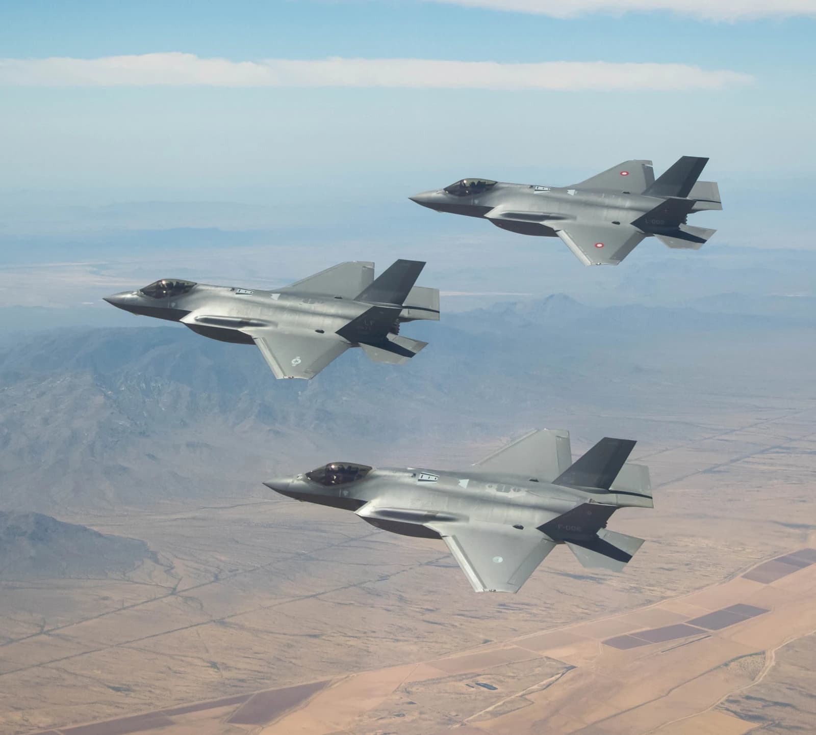 Three F-35A fighter jets flying in formation over a desert landscape.