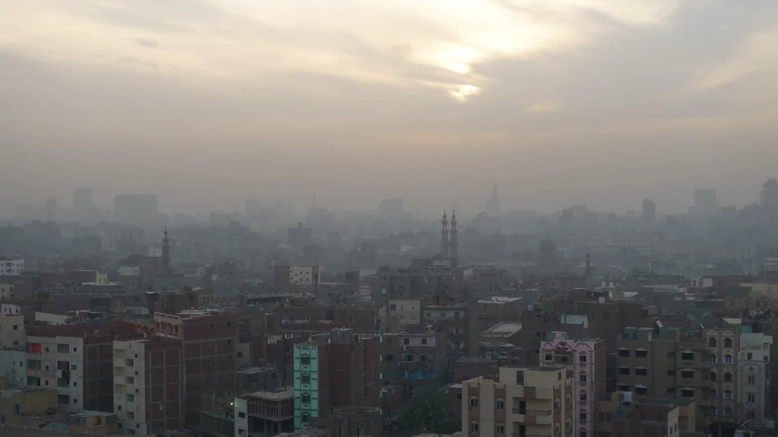 Panoramic view of Cairo, Egypt, showing a dense urban landscape under a hazy sky.
