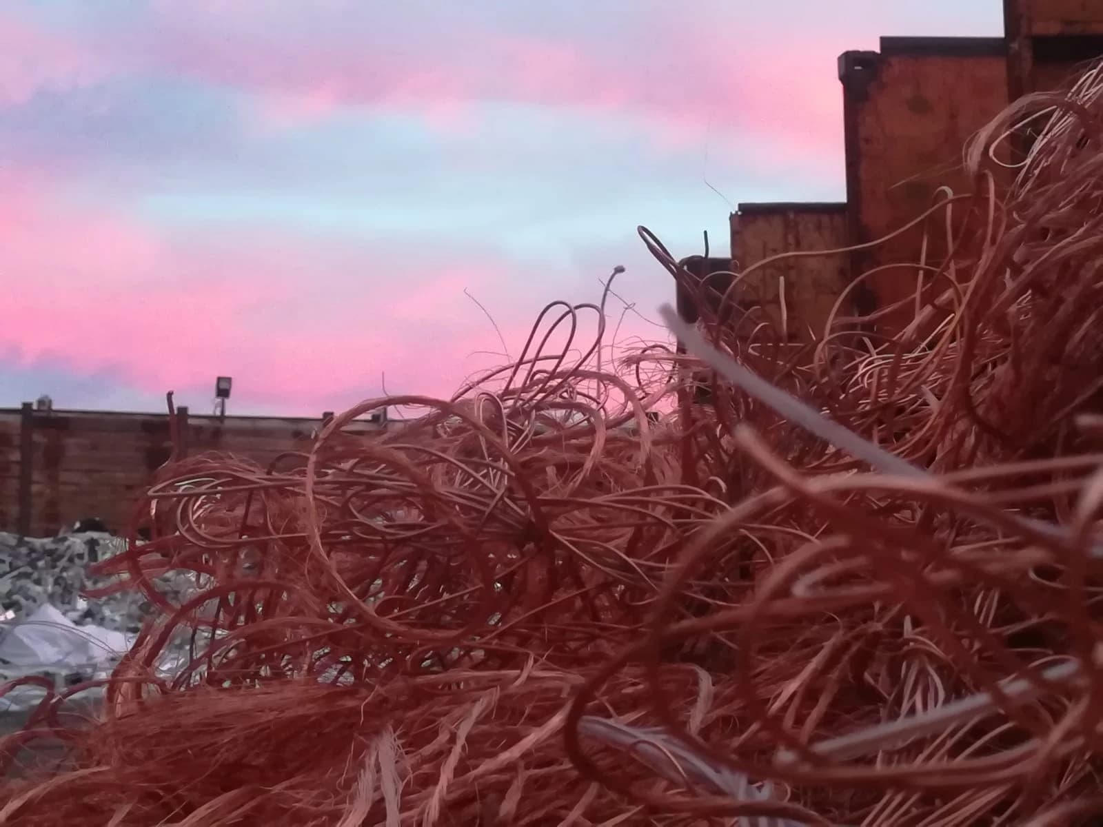 Close-up of a large pile of scrap copper wiring with industrial buildings in the background.