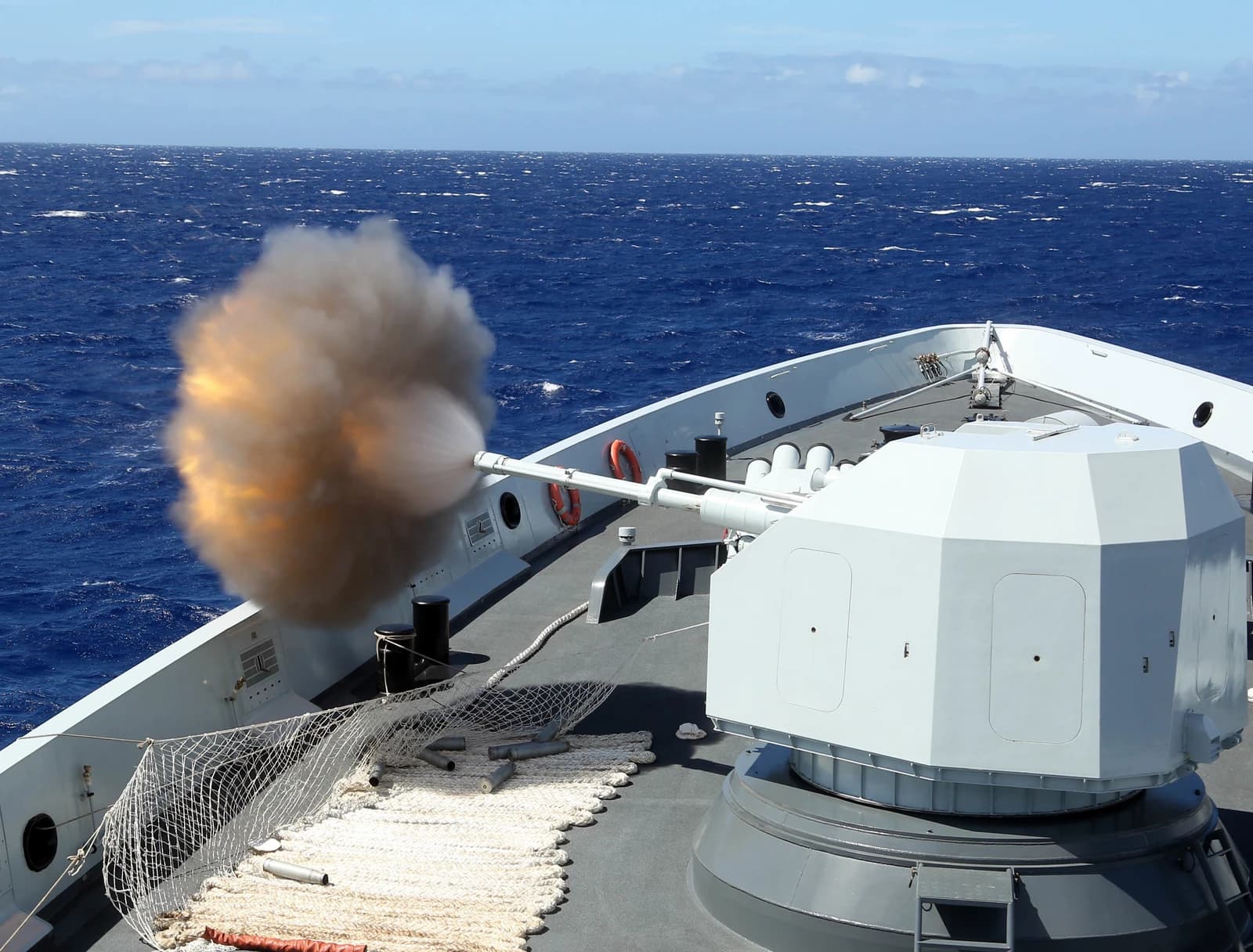 Chinese warship firing its main deck gun, muzzle flash visible.