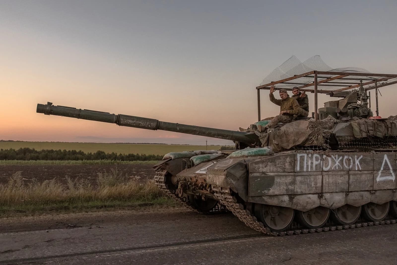 Soldiers riding on top of a T-90M Proryv tank in a rural landscape.