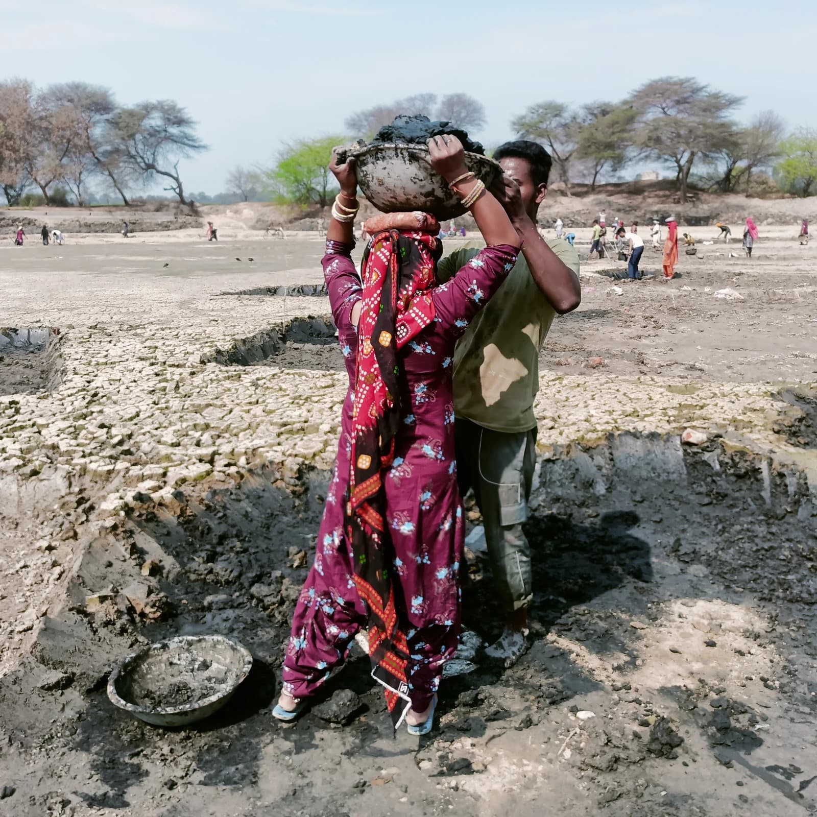 MGNREGA workers removing mud from a dry pond in a rural area.