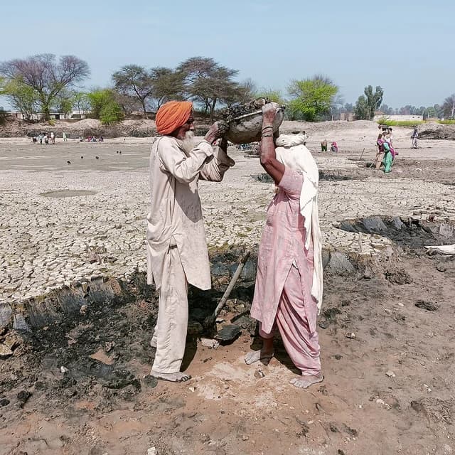 Man in orange turban and woman moving earth with a basket on her head.